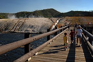 People walking on a bridge over Firehole River towards Excelsior Geyser Crater