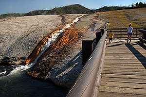 People walking on a bridge over Firehole River towards Excelsior Geyser Crater